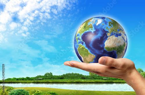 Man hand with earth globe on it and a beautiful green landscape