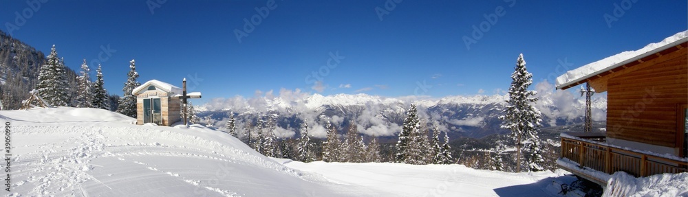 Small snowy chapelle with wooden cross in the mountains panorama