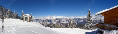 Small snowy chapelle with wooden cross in the mountains panorama