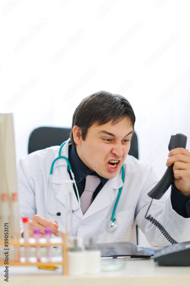 Angry medical doctor shouting in phone handset Angry medical doctor shouting in phone handset