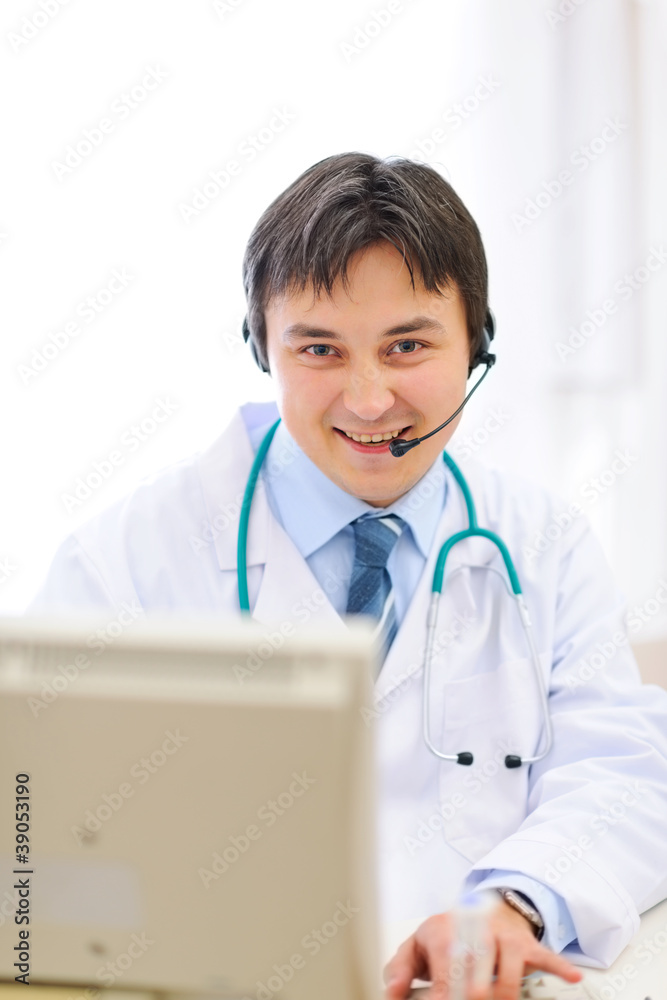 Smiling medical doctor with headset working on pc