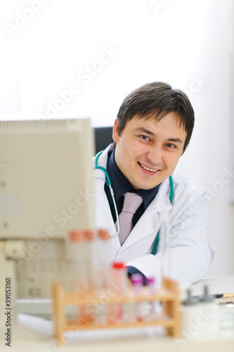 Smiling medical doctor looking out from computer at office