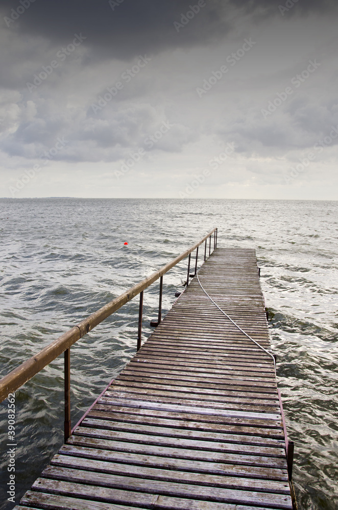 Obraz premium Wooden bridge on wavy lake. Dark sky before storm