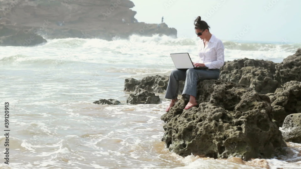Businesswoman working on laptop on the rocks by the sea Businesswoman working on laptop on the rocks by the sea