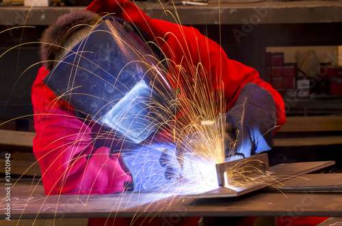 Welder in red overalls creates sparks.   