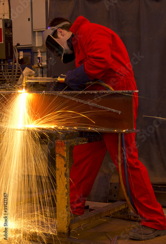 Welder in red overalls cuts metal.