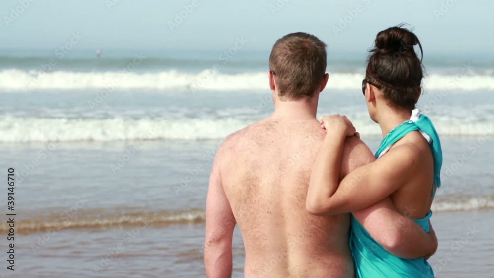 Couple hugging and looking at the surfers in the sea