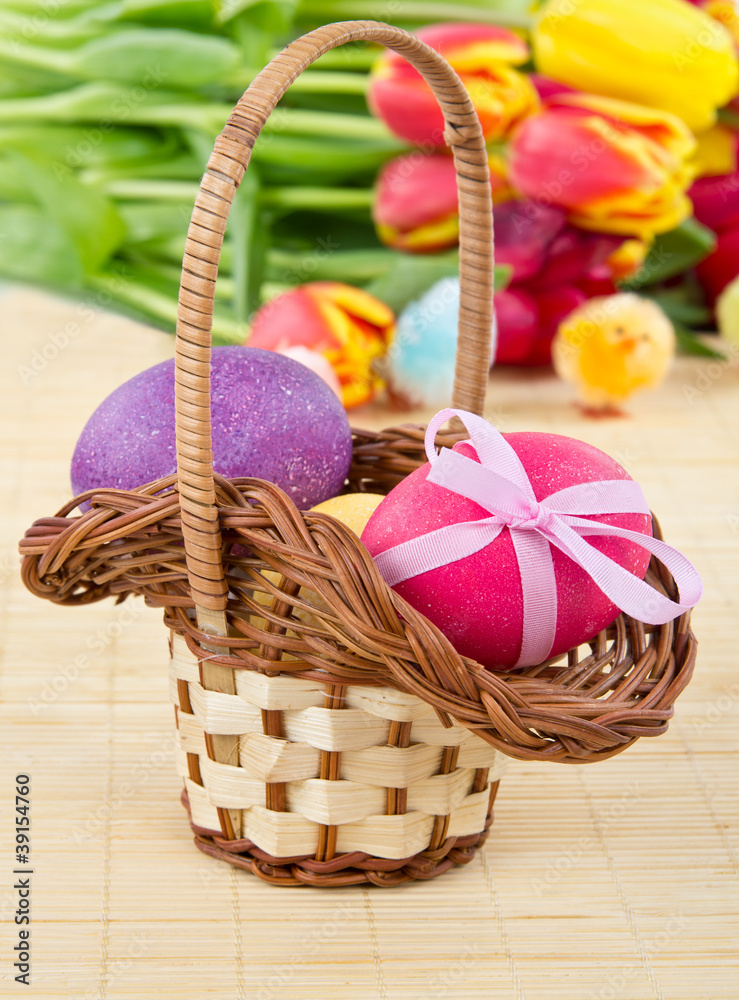 Easter eggs in basket with tulips on background