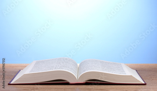 Open book on wooden table on blue background