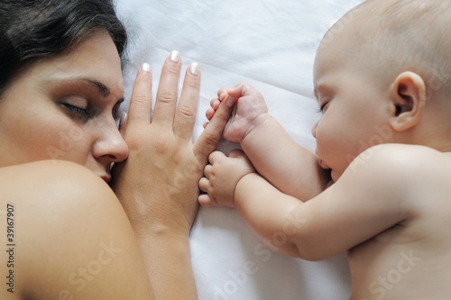 Baby sleeping close to her mother, holding her finger photo