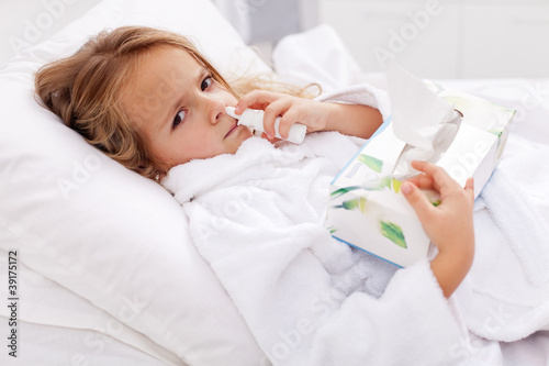 Billede på lærred Little girl with bad cold - using nasal spray and paper napkins