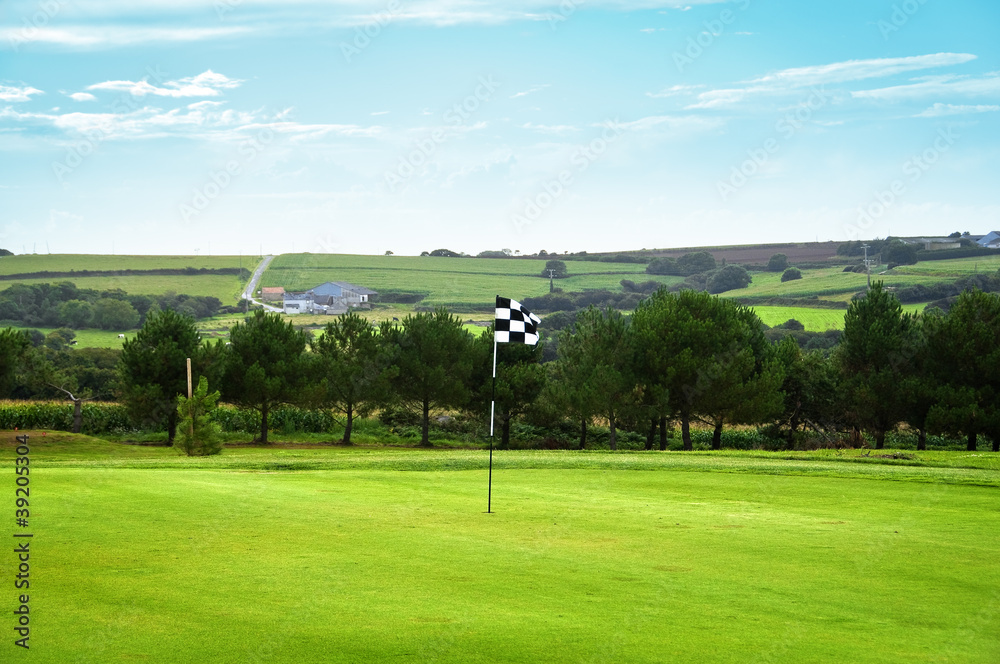 Obraz premium Golf green with a checkered flag, the countryside in background