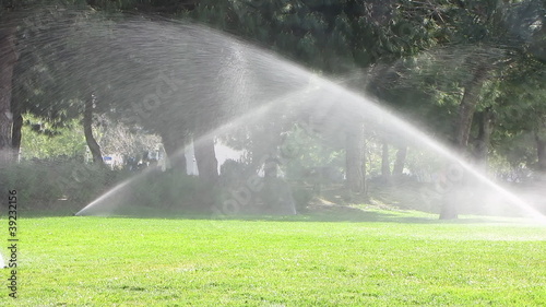 Water sprinkler showering grass in park