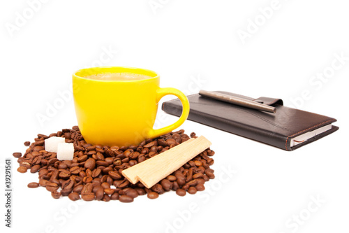 Yellow cup of coffee stands before deferred notebook