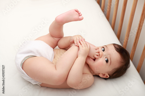 Cute baby sucking his toes in cot
