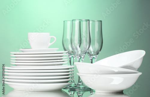 Clean plates, cup and glasses on green background