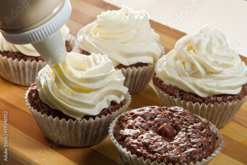 Decorating chocolate muffin with vanilla cream