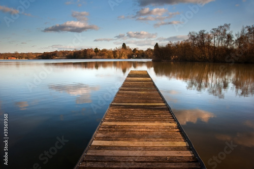 Landscape of fishing jetty on calm lake at sunset with reflectio