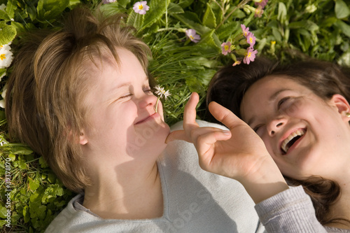 A girl with Down syndrome and her sister laughing in the grass.