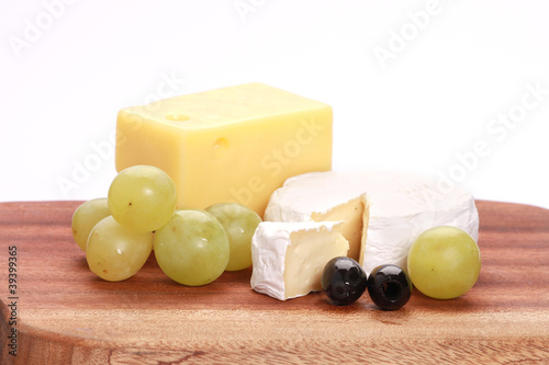 cheese on wooden plate with olives and grapes