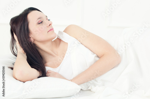 Young caucasian woman with long dark hair relaxing in bed