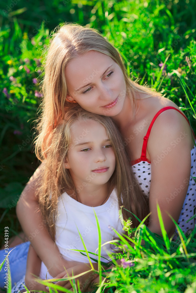 Beautiful mother and daughter sitting on green lush grass meadow Beautiful mother and daughter sitting on green lush grass meadow