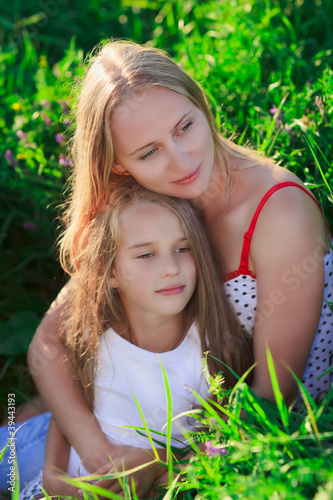 Beautiful mother and daughter sitting on green lush grass meadow