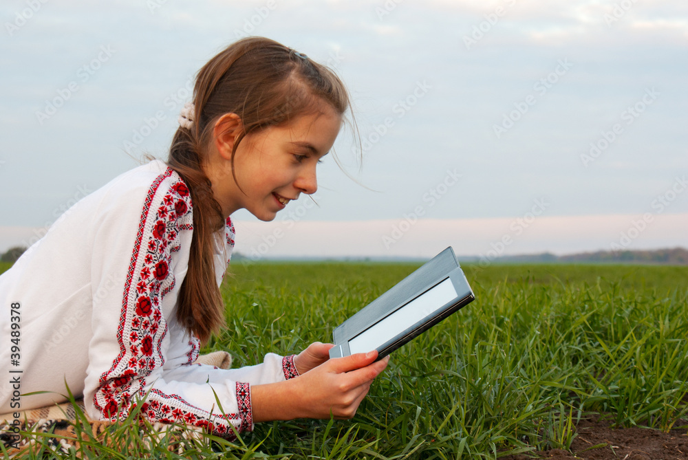 Teen girl with electronic book laying on grass