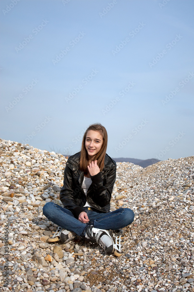 Teenage girl with rollerblades sitting on pebbles Teenage girl with rollerblades sitting on pebbles