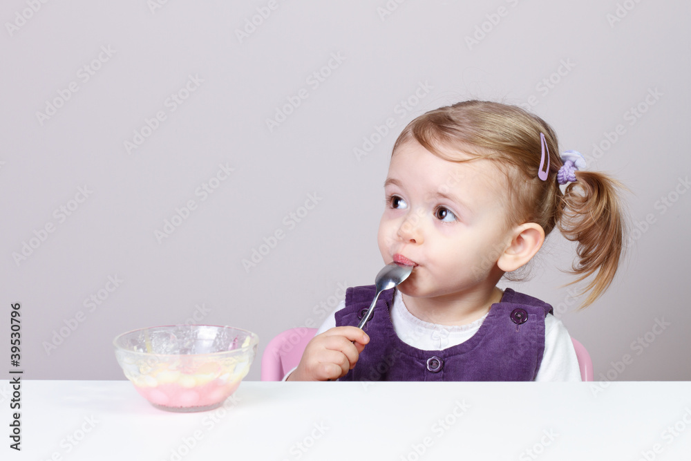 Adorable little girl eating creamy pudding with spoon Adorable little girl eating creamy pudding with spoon
