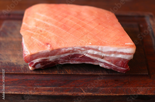 Pork belly with scored skin, uncooked on a wooden cutting board