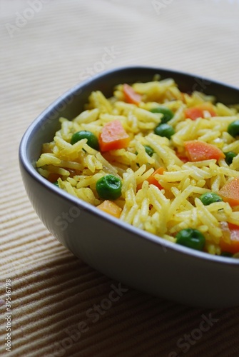 A bowl of yellow basmati rice with carrots, peas and curry