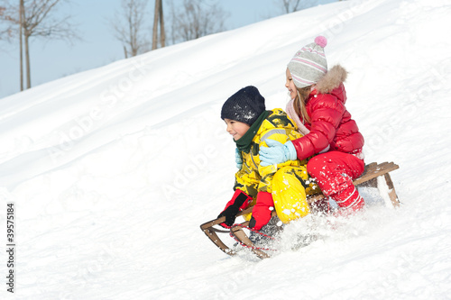 Two kids sliding with sledding in the snow.