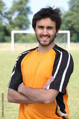 Footballer with arms crossed standing on pitch