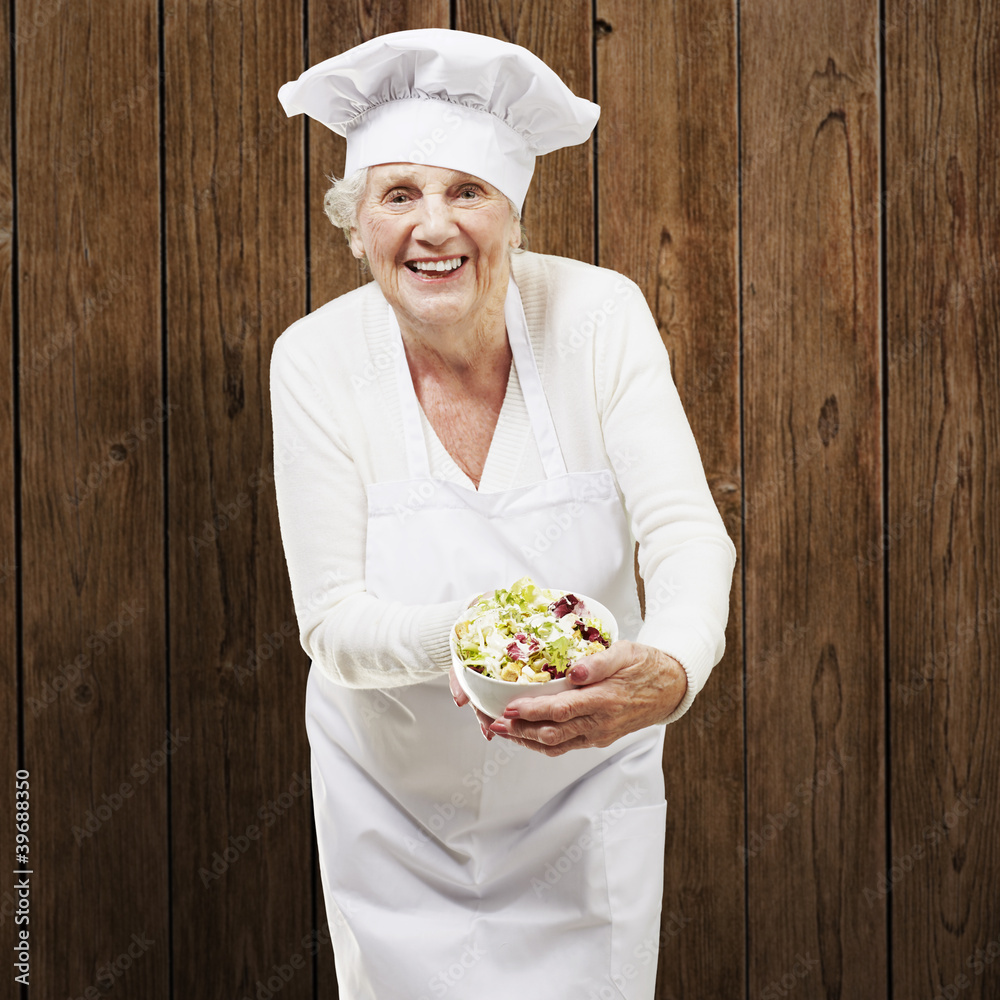 senior woman cook holding a bowl with salad against a wooden bac senior woman cook holding a bowl with salad against a wooden bac