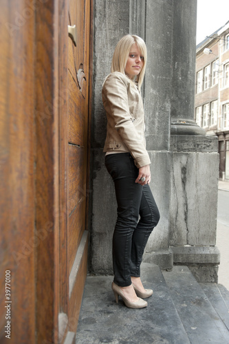young blond woman standing against a door