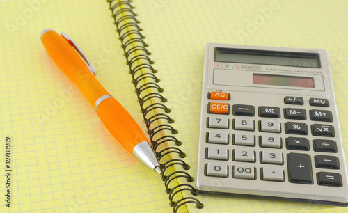 Old calculator and pen on the yellow writing-book