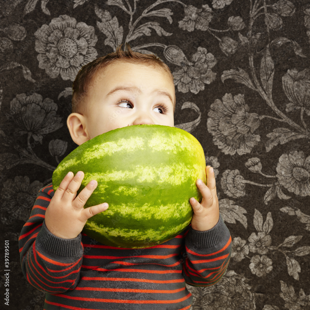 Fototapeta premium portrait of a handsome kid holding watermelon and sucking agains