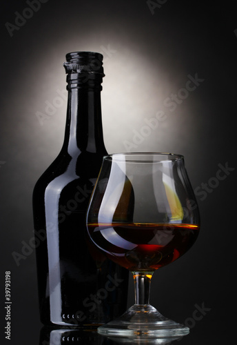 Glass of brandy and bottle on gray background