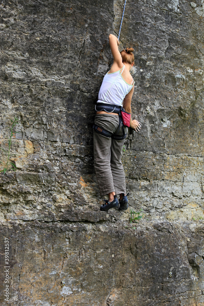 Female rock climber clinging to a cliff on her way up