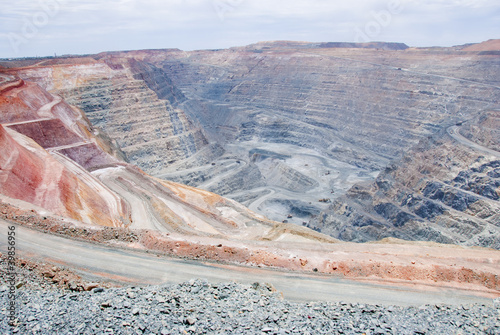 Big mine pit with little dump trucks and reddish soil
