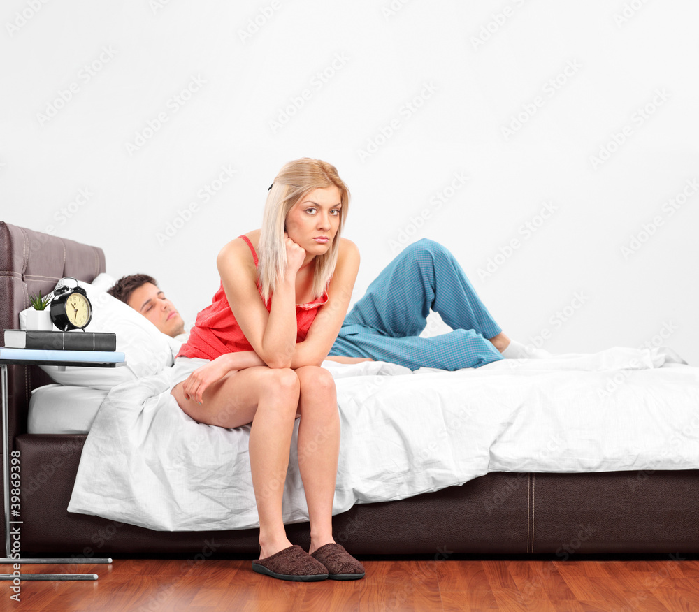 Obraz premium Disappointed blond female sitting on a bed while her boyfriend i