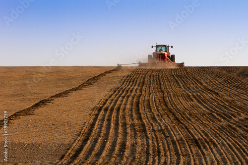 Agricultural tractor sowing seeds and cultivating field. Arable land, rear view of tractor on a sunny day and space copy for text