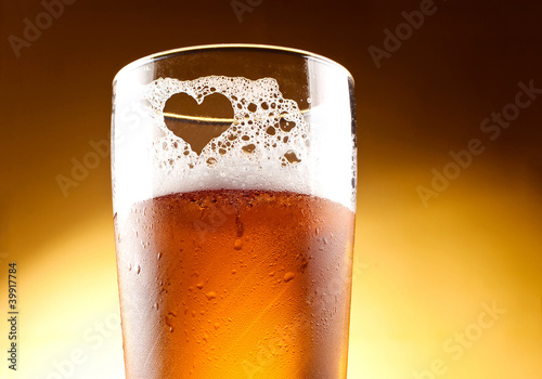 Glass of beer with the heart represented with froth close up ove