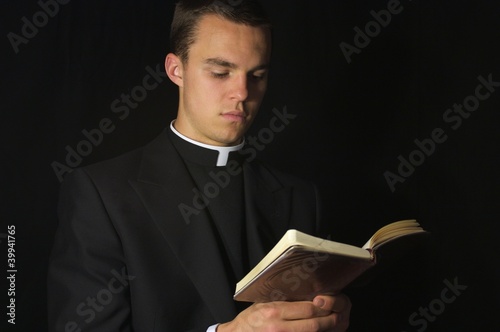 Young Priest in black reading prayer book