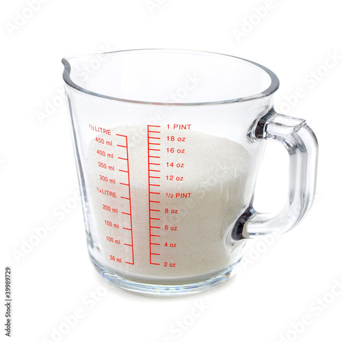 Sugar in measuring cup isolated on white background