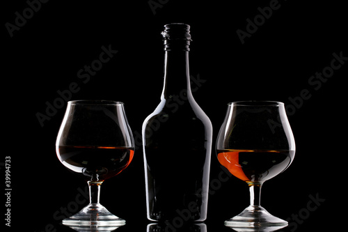 Glasses of brandy and bottle on black background