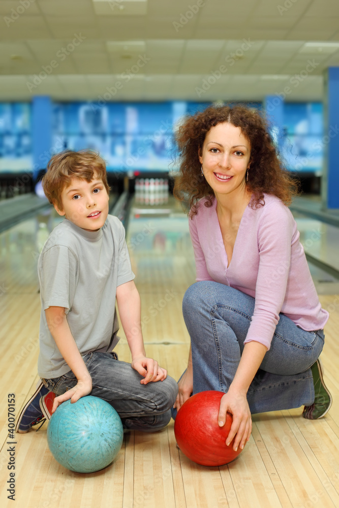Fototapeta premium mother and son keep balls ant sit on floor in bowling club