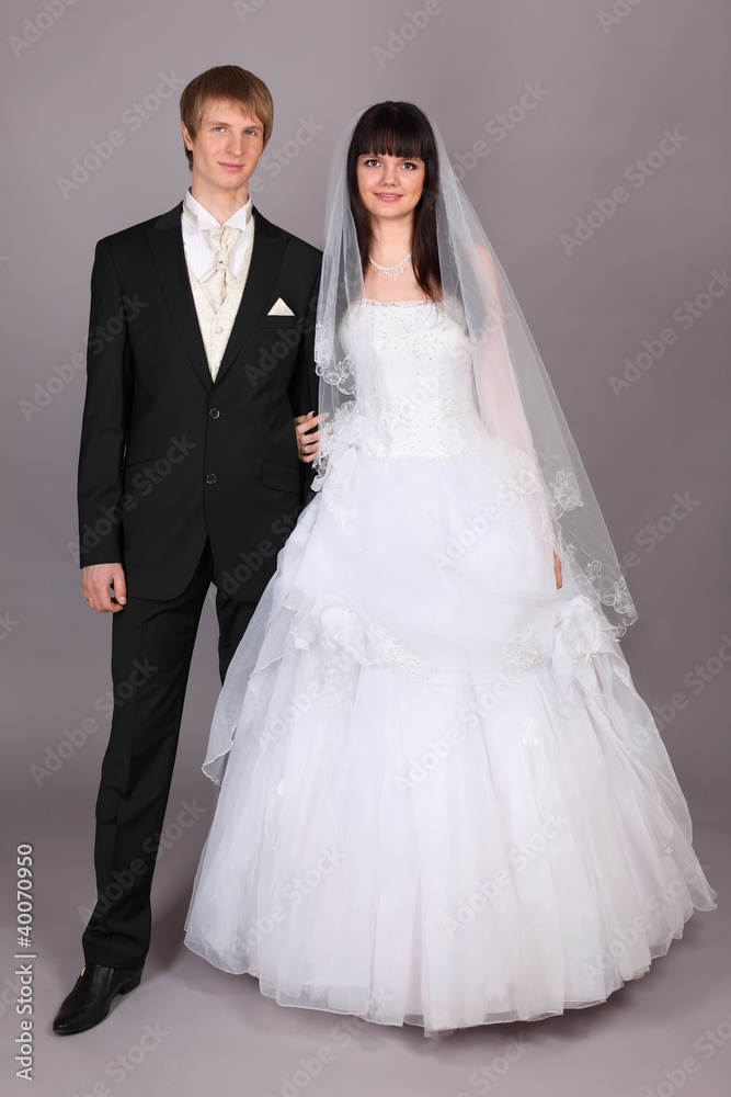 Happy young groom and beautiful bride in studio on gray