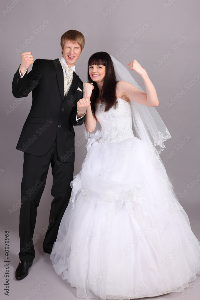 Young groom and beautiful bride are very happy in studio on gray